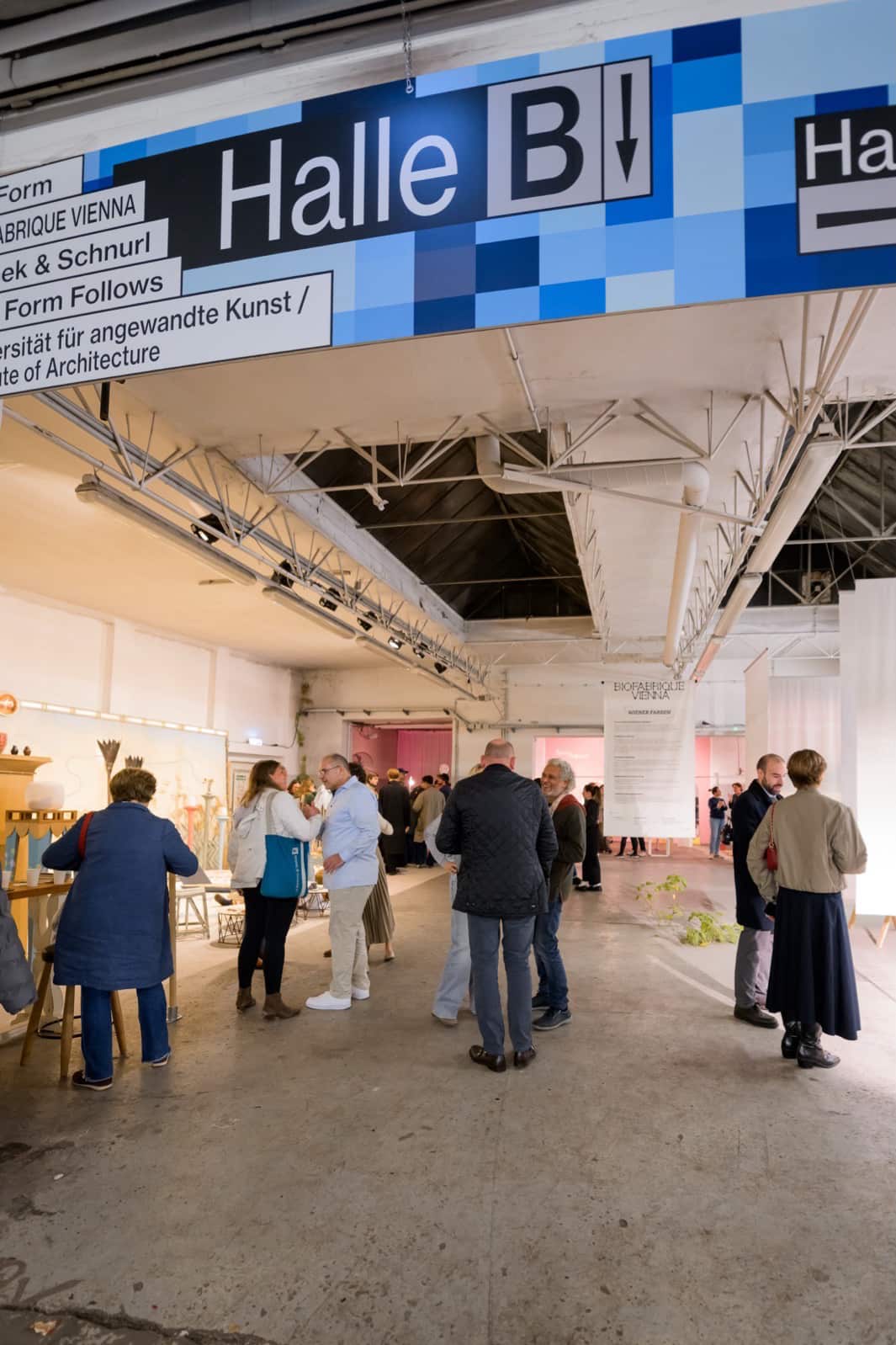 Exhibition shot of the Vienna Design Week; people standing around the room, a big banner above them marking Hall B.