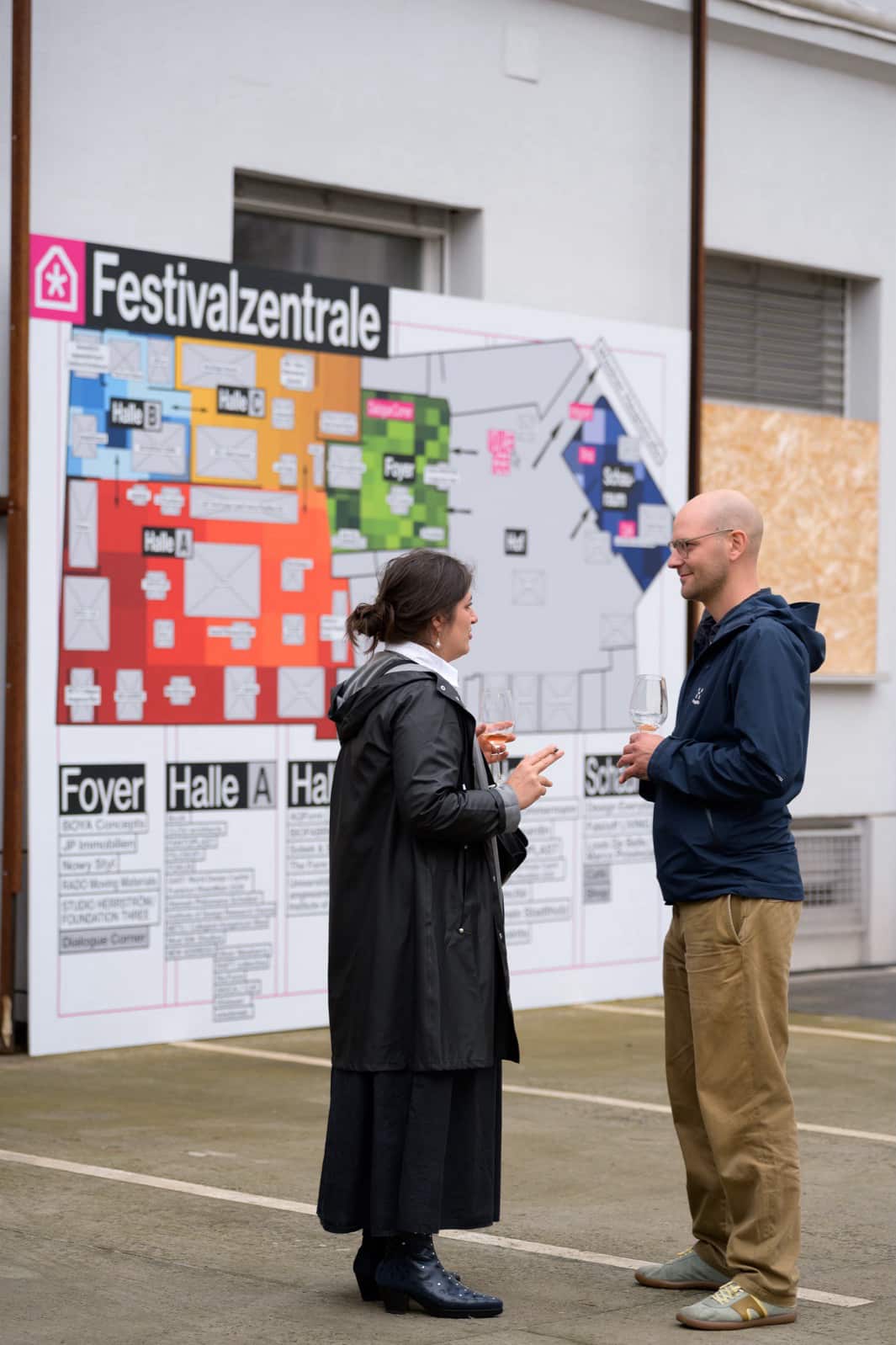 Photo of two people conversing in front of a big oversight poster of the Vienna Design Week venue.