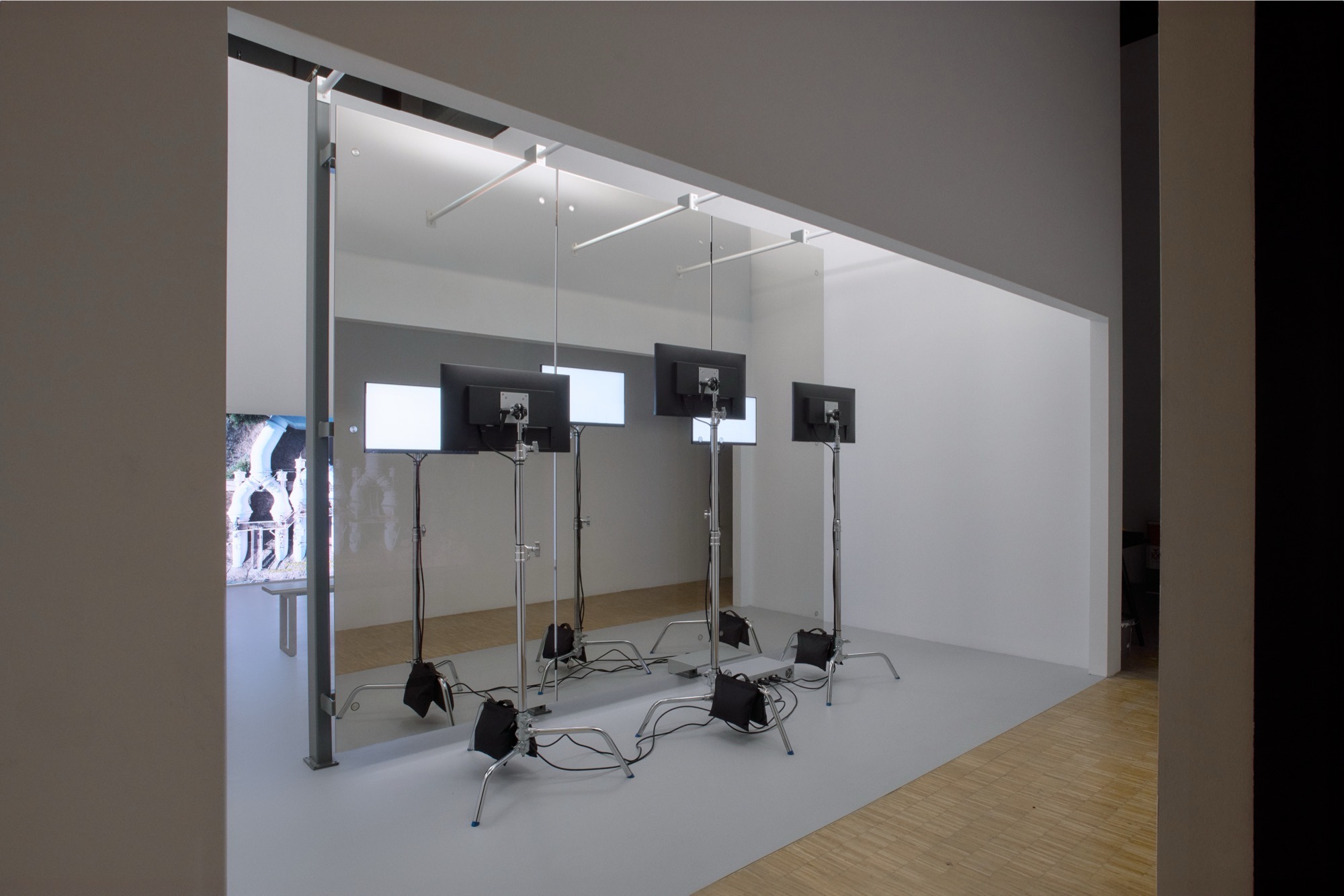 Exhibition View of 3 monitors seen from behind, reflected in a big mirrored wall